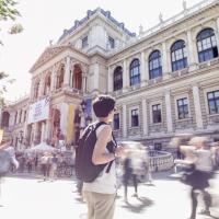 Foto einer Studentin vor der Universität Wien. Sie ist scharf zu sehen, alle anderen sind verschwommen. Es entsteht ein Eindruck von Orientierungslosigkeit