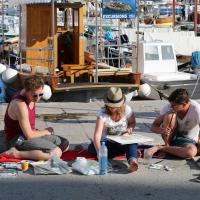 Foto von 3 malenden Personen, sitzend auf dem Boden in einem Hafen