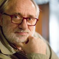 Ein Foto von Giorgos Chondors. Er schaut nachdenklich in die Kamera. Er trägt eine rote Brille und hat einen grauen, dünnen Vollbart. 